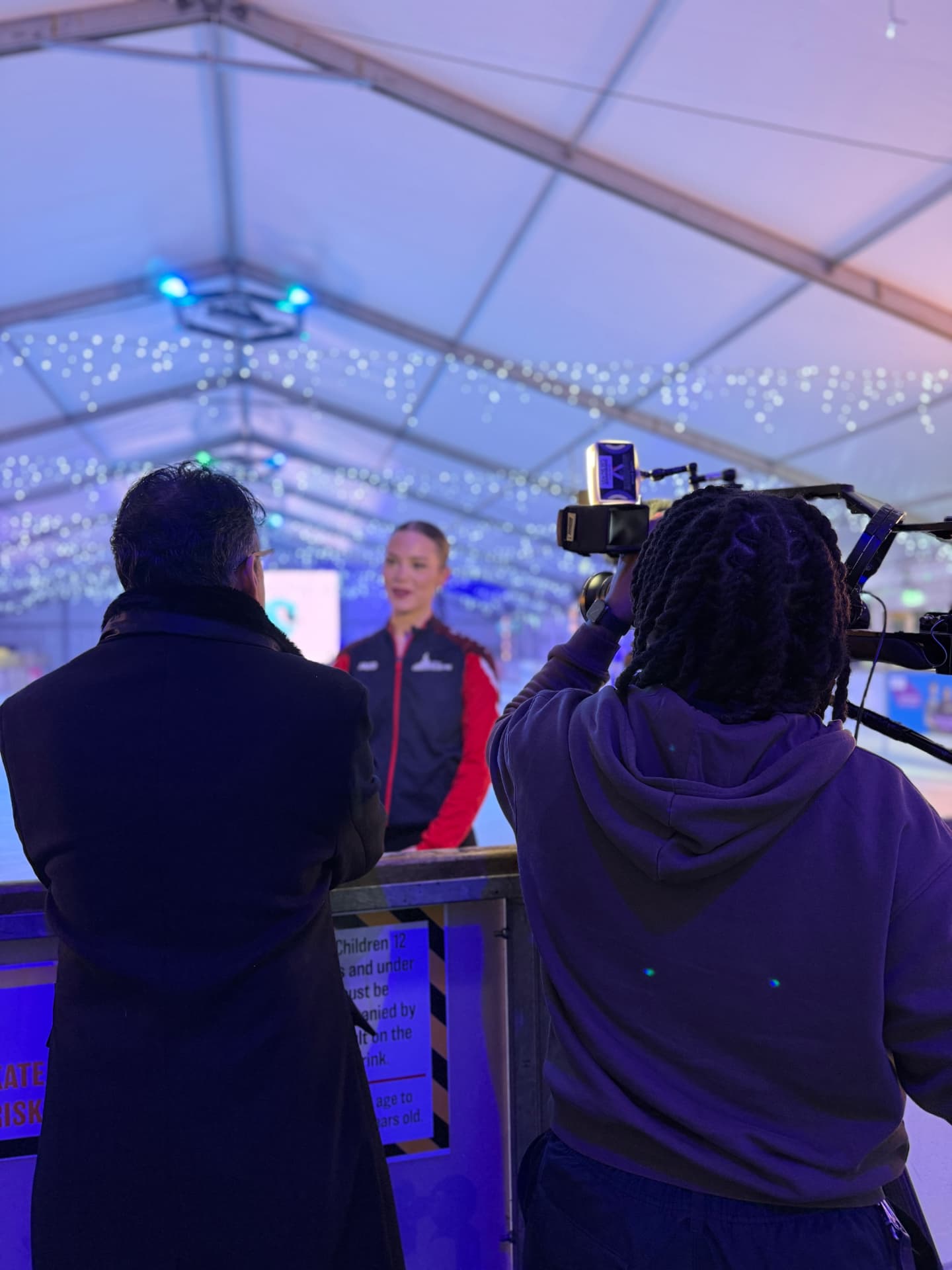 A camera operator filming an interview with a skater at an ice rink